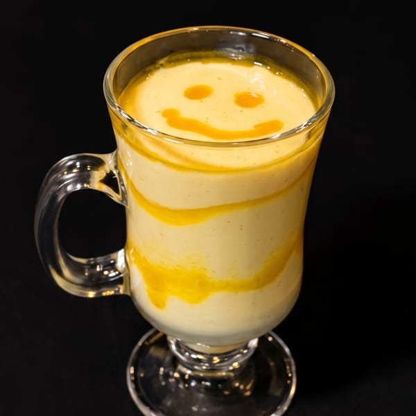 Creamy yellow drink in a glass mug, topped with an orange smiley face.
