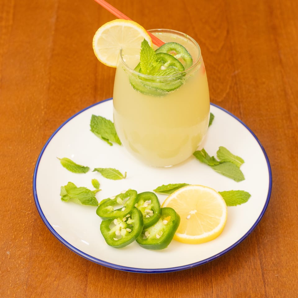 A glass of lemonade garnished with lemon, mint, and jalapeño slices on a white plate.