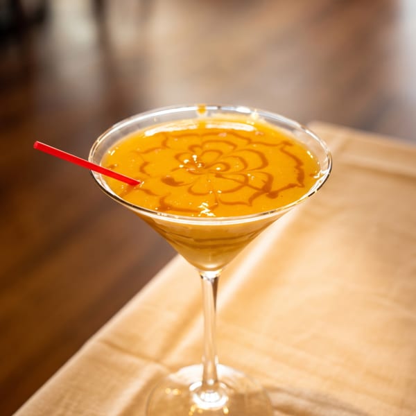 Orange drink in a martini glass with a red straw and decorative sauce swirl on a light tablecloth.